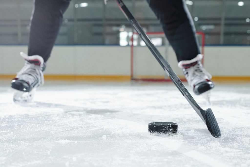 Legs of male hockey player in sports uniform and skates moving down ice rink