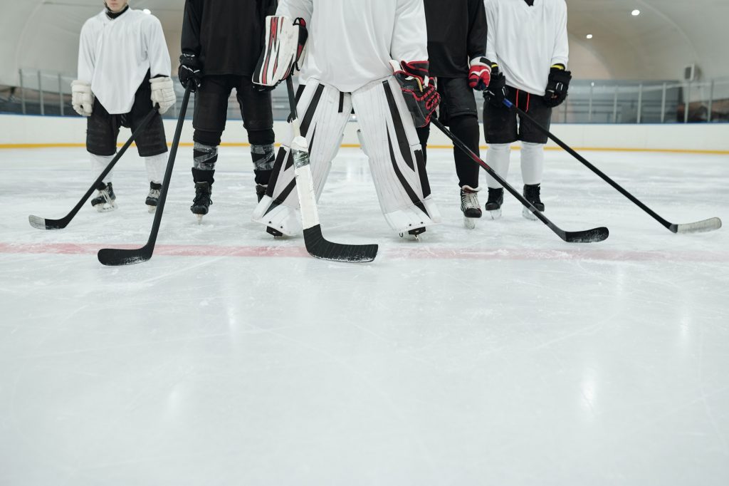 Low section of several hockey players and their trainer with sticks on ice rink