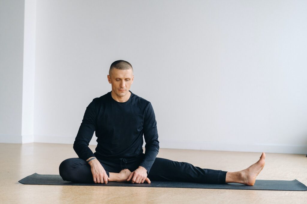 A man in sports clothes trains lying down, doing stretches in the gym
