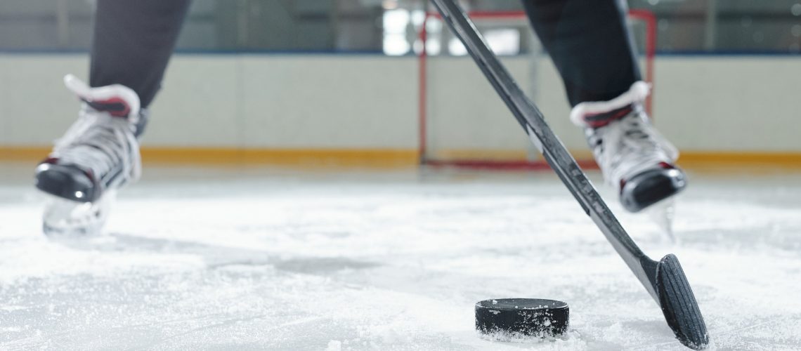 Legs of male hockey player in sports uniform and skates moving down ice rink